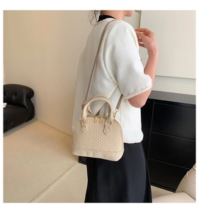 Detail of cream-colored shell bag featuring crocodile embossed leather and gold zippers