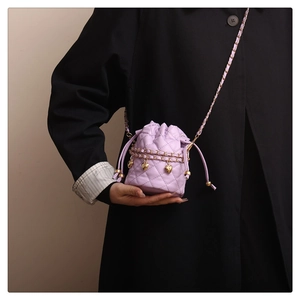 Detail der lila gesteppten Eimertasche mit Goldkette und Herzanhängern für Damen