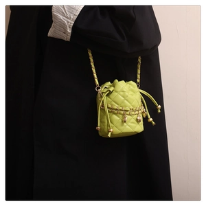 Détail d'un sac seau matelassé vert fluo avec chaîne dorée et pendentifs en cœur