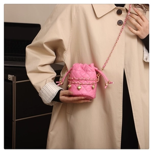 Détail du sac seau matelassé rose avec charms cœur dorés et bandoulière sur manteau beige