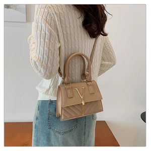 Detail of a beige quilted crossbody bag with gold V-logo and tassel on a wooden table