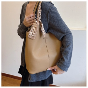 Detail of khaki tote bag featuring lychee grain leather and checkered silk ribbon handle