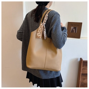 Detail of tan pebble leather tote bag featuring a decorative scarf wrapped on the handle