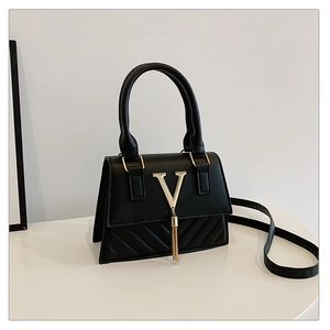 Detail of black quilted crossbody bag with golden V-logo and decorative tassel