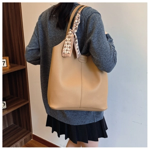 Detail of khaki leather tote with wide strap and fashion tag in an indoor setting
