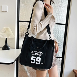 Black canvas tote bag with white lettering and wide strap in casual street style
