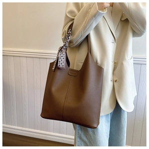 Detail of a dark brown lychee leather tote bag featuring a geometric silk scarf accessory