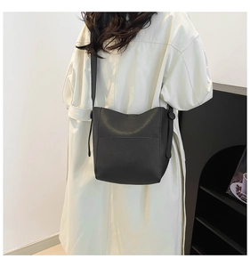 Detail view of dark grey textured leather bucket bag with wide strap on model