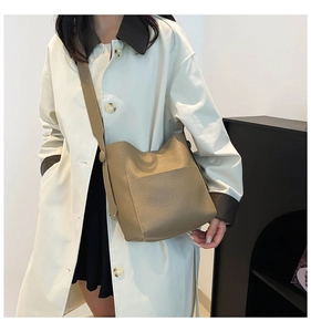 Detail of khaki lychee grain leather bucket bag with wide strap on trench coat