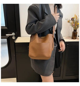 Close-up of brown litchi pattern leather bucket bag with wide shoulder strap on model