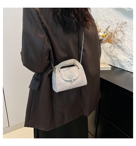 Chic silver crossbody bag with heart clasp and chain strap worn by a model in dark coat