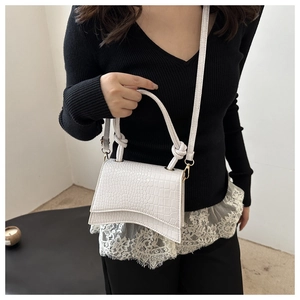 Detail of white crocodile embossed handbag with unique curved base and knotted handle