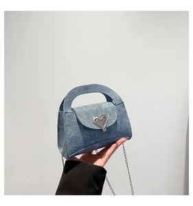 Detail of blue denim mini crossbody bag with a heart-shaped silver metal clasp and chain