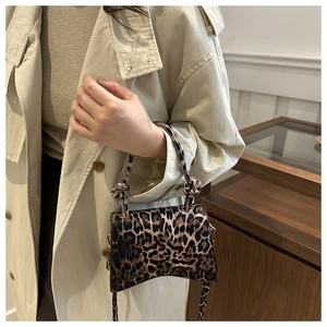 Détail du mini sac à main léopard avec base incurvée porté sur un trench-coat beige