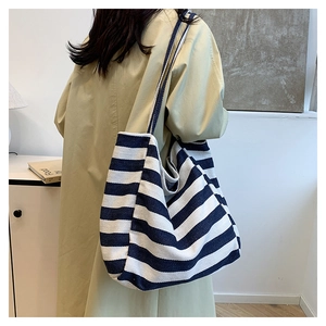 Detail of wide striped canvas tote bag straps shown on a beige trench coat