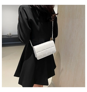 Quilted white crossbody bag with silver chain strap shown against a dark coat