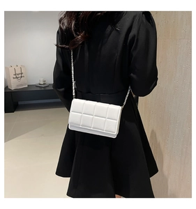 Rear view of a white quilted crossbody bag with metal chain strap on a black dress