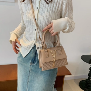 Beige leather crossbody bag with V-quilt stitching and gold tassel charm on model