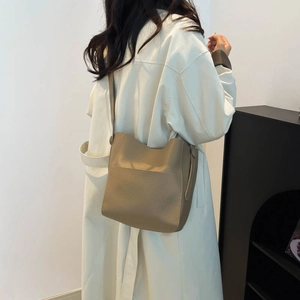 Minimalist khaki lychee texture leather bucket bag worn by model in a modern interior setting