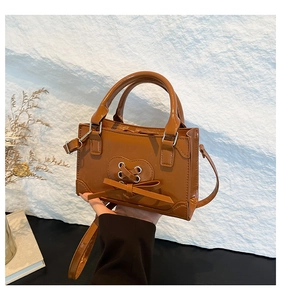 Detail of a brown glossy leather crossbody bag with heart lacing and a bow ornament