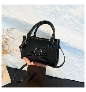 Detail of black crossbody bag featuring a chic heart ribbon bow and adjustable strap