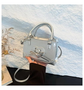 Detail of silver mini square bag featuring heart patch and bow design with metallic finish