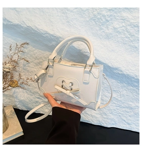 Detail of white mini crossbody bag featuring heart cutout design and decorative bow