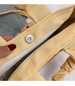 Detail view of the silver magnetic snap closure on a beige canvas bucket bag with stitching