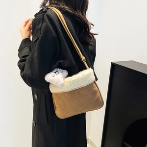 Sac bandoulière en daim marron et fausse fourrure avec peluche sur un manteau noir