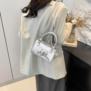 Silver metallic leather handbag with heart cutout and bow detail, worn as a shoulder bag