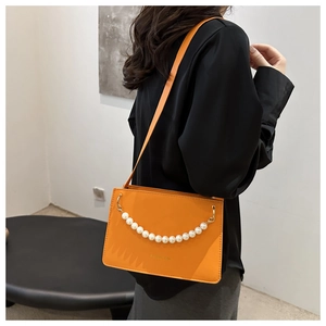 Detail showing bright orange rectangle shoulder bag with elegant large white pearl chain