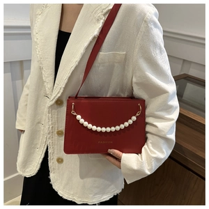 Detail of red leather crossbody bag with pearl chain and fashion text on white suit