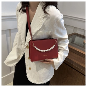 Detail of red square crossbody bag with white pearl chain and golden Fashion text