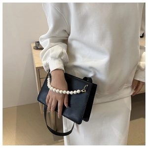Detail of chic black rectangle bag featuring a luxury pearl handle strap and gold buckles