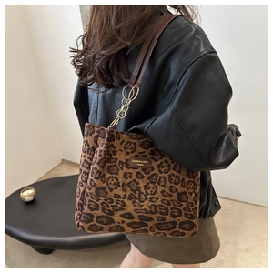 Detail of leopard print tote bag featuring leather logo patch and gold chain strap accent