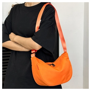 Detail of a bright orange crescent crossbody bag with adjustable strap worn by a model