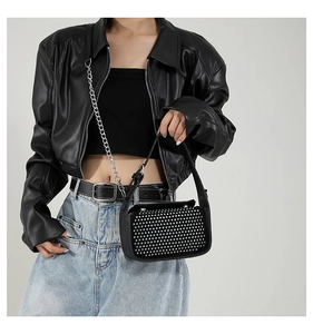 Detail of black crossbody bag featuring silver stud rivets and a thin metal chain strap