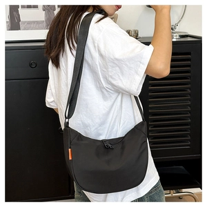 Detail view of black nylon crescent bag with adjustable strap and orange side label