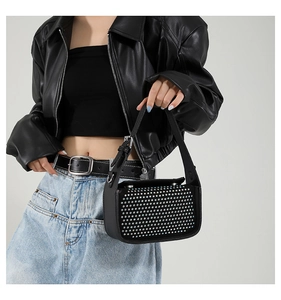Close-up of black handbag with silver rivet studs and wide strap shown on model