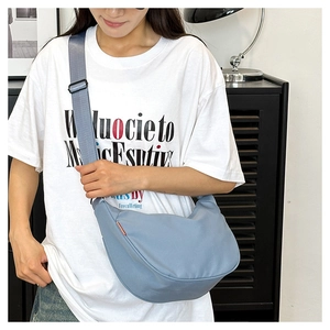 Detail shot of light blue dumpling bag with wide adjustable strap and side red label