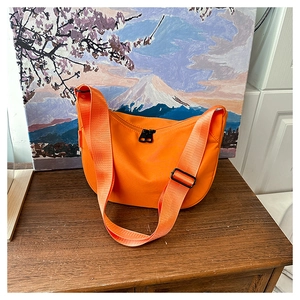Macro detail of orange nylon crescent bag with adjustable strap on a wooden table