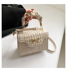 Detail of cream pleated handbag featuring a gold bow buckle and elegant ruched top handle