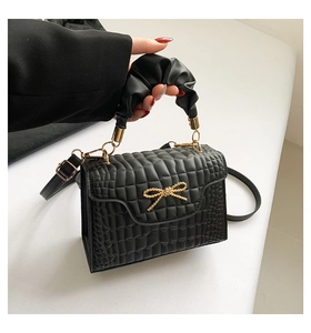 Detail of black crocodile texture handbag with gold bow and pleated handle