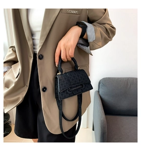 Detail of black mini crossbody bag with embossed texture and gold hardware on model