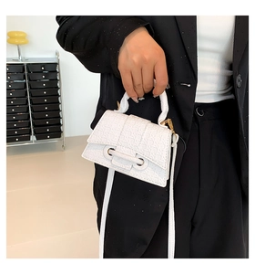 Detail view of the geometric embossed texture and golden metal buckle on a white mini handbag