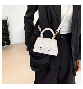 Detail of white hourglass bag with woven texture, top handle, and golden metal hardware