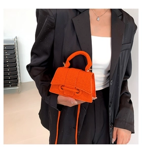 Detail of orange hourglass handbag with woven texture held by a model in a black blazer