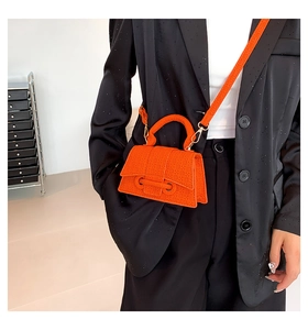 Detail of bright orange textured crossbody bag on model in black suit jacket