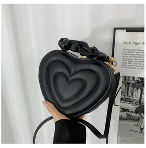 Close-up of black heart-shaped crossbody bag with quilted patterns and ruched handle