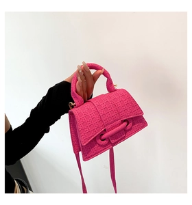 Detail of vibrant hot pink crossbody bag with woven texture held by a model